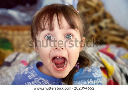 Shocked screaming little girl with opened mouth in her bedroom