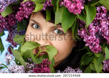 Beautiful young model woman with lilac bouquet and wreath as flowers hair style on blue background