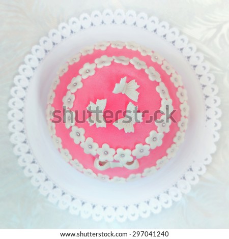 Top view of a pink cake with butterflies in a white plate over a white tablecloth