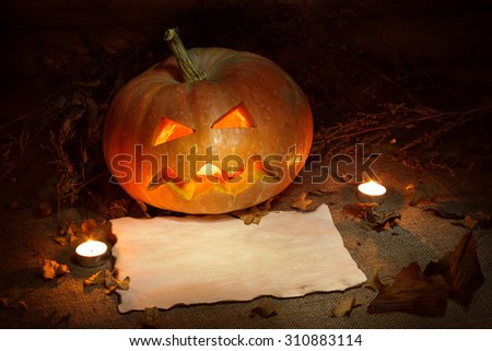 Scary Halloween pumpkin and old burned paper ad layout with candlelight and autumn leafs. Still life. Wooden background.