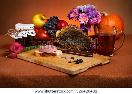 Still life with bitten sandwich on wooden cutting board, tumbler of tea, jar of jam and harvested autumnal fruits and vegetables. Simple breakfast.