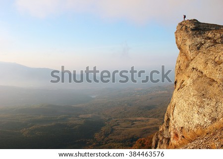 Woman trekker stands on edge of the cliff looking over misty valley