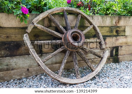 a broken wooden wheel by fence