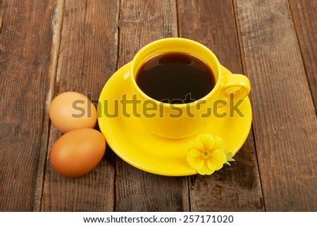 A cup of coffee, flower and eggs on a wooden table background