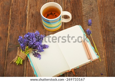 Notebook on a wooden table background with a bouquet of hyacinth flowers and a cup of tea
