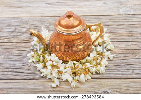 Copper kettle with tea acacia flowers on a wooden table background
