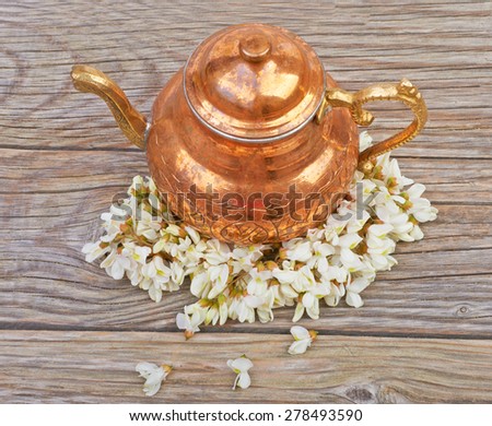 Copper kettle with tea acacia flowers on a wooden table background