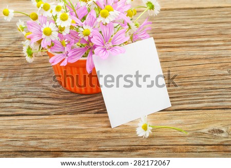 Flowers and a white blank sheet of paper on a wooden background