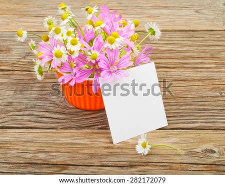 Flowers and a white blank sheet of paper on a wooden background