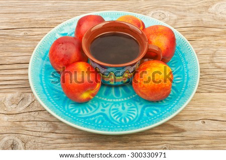 Cup of coffee and ripe nectarines with water drops in a wicker plate on old wooden table. health and diet food