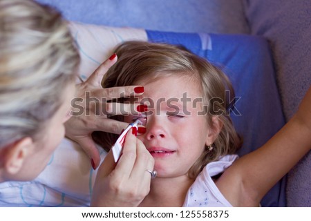 Mom puts the child in the eye cream,best focus on the face of the child and the mother\'s left hand,Blurred head mother
