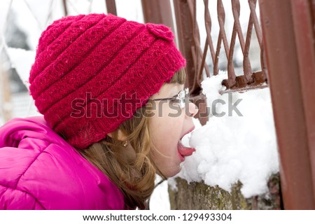 child with glasses licking snow, best focus on the cap, the hair, face and glasses