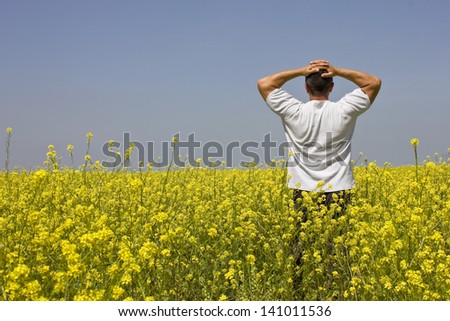man standing in a field of flowers, best focus on oilseed rape around the man and the hands