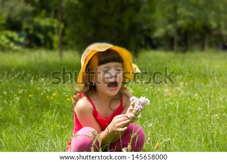 child sits in grass and sneezes,best focus on his right hand, a bouquet of flowers, lips, face soft focus, blurred background