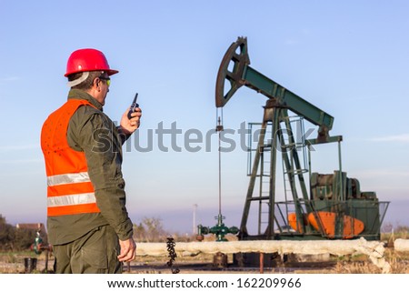 Oil Industry Pump Jack With One Oil Worker Who Using A Portable Radio.
