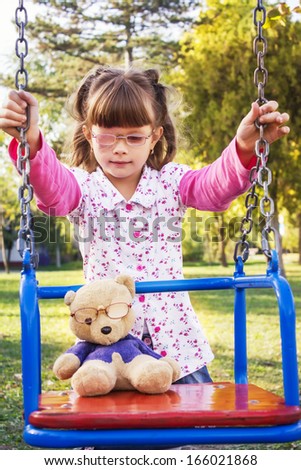 girl sick eyes  playing with a teddy bear on a swing,best focus on hair girls,blurred motion,background blurred, bear soft focus