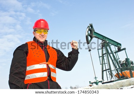 worker on an oil pump holds a clenched fist,best focus on the helmet and vest, soft focus oil pump