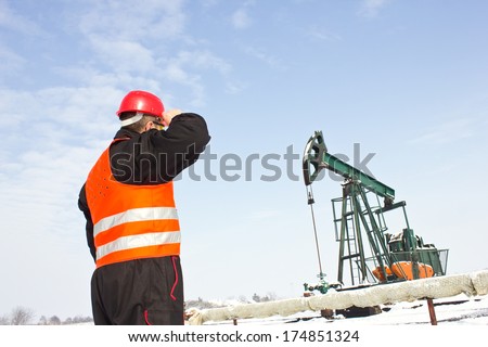 worker on an oil pump with his back hand holding the helmet,best focus on the helmet and vest, soft focus pump