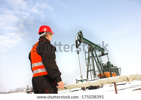 Oil Industry Pump jack with one oil worker in an orange vest with hand radio station,best focus on the helmet and vest, pump soft focus
