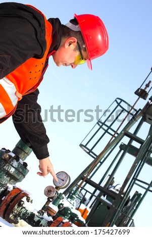 worker on an oil pump points a finger manometer, best focus face helmet and vest, soft focus pump