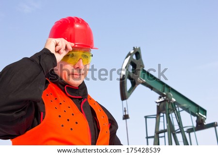 worker on an oil pump keeps the helmet with his hand,best focus face helmet and orange vest, soft focus pump