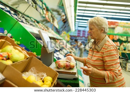 Elderly woman weighing goods on digital weight in supermarket, shopping for fruits and vegetables in produce department of a grocery store/supermarket (color toned image)