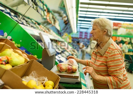 Elderly woman weighing goods on digital weight in supermarket, shopping for fruits and vegetables in produce department of a grocery store/supermarket (color toned image)