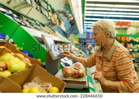 Elderly woman weighing goods on digital weight in supermarket, shopping for fruits and vegetables in produce department of a grocery store/supermarket ( color toned image )
