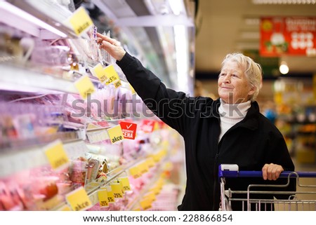 Elderly woman choosing dairy produce in supermarket, shopping for dairy produce  in department of a grocery store/supermarket ( color toned image )