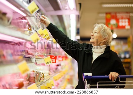 Elderly woman choosing dairy produce in supermarket, shopping for dairy produce  in department of a grocery store/supermarket ( color toned image )