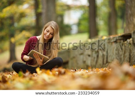 Young woman using tablet outdoor sitting on grass and smiling. Girl using digital tablet pc in the park. Student using tablet after school.