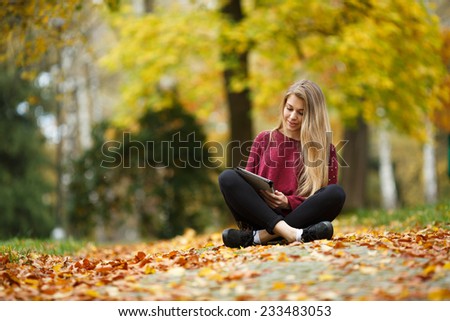 Young woman using tablet outdoor sitting on grass and smiling. Girl using digital tablet pc in the park. Student using tablet and laughing.