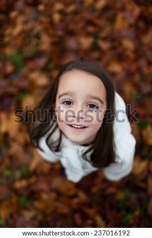 Cute close up portrait of little girl standing on colorful leaves outdoor in fall. Forest foliage. Smiling happy and excited. Entertainment in autumn outdoors.