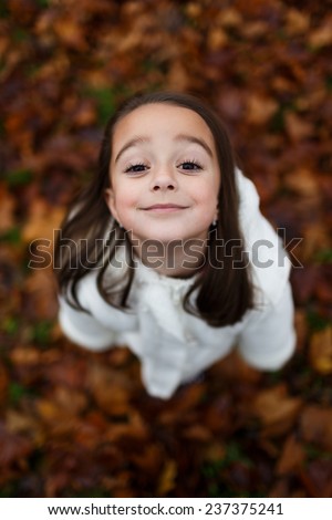 Cute close up portrait of little girl standing on colorful leaves outdoor in fall. Forest foliage. Smiling happy and excited. Entertainment in autumn outdoors.Beautiful adorable wench.
