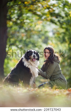 Beautiful brunette girl with her Dog in Autumn park. Bernese Mountain Dog. Woman with dog in autumn outdoors. Friendship in fall. Girl hugging and embracing her dog.