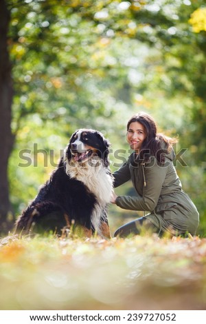 Beautiful brunette girl with her Dog in Autumn park. Bernese Mountain Dog. Woman with dog in autumn outdoors. Friendship in fall. Girl hugging and embracing her dog.