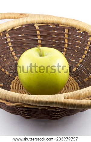 One single green apple in the center of a wicker basket isolated on white