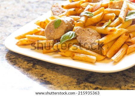 Sliced sausage with penne pasta and red tomato sauce with basil leaves