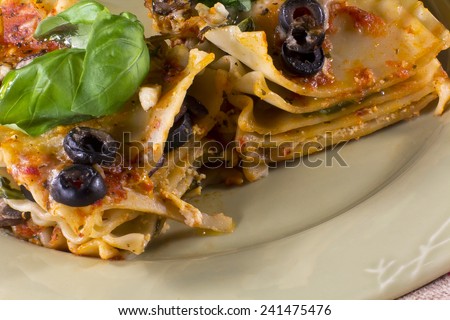 Vegan or vegetarian lasagna dinner topped with mushrooms, olives, artichoke hearts, and fresh basil