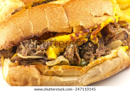 A messy Philly Cheesesteak with onions peppers and mushrooms, onion rings on the side