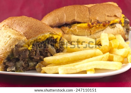 A messy Philly Cheesesteak with onions peppers and mushrooms, fries on the side