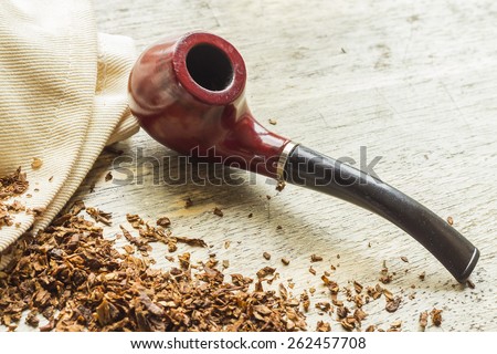 Tobacco pipe on rustic warn wood surface with spilled natural tobacco