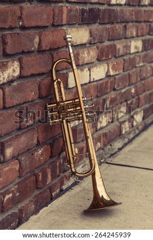 Old worn trumpet stands alone against a brick wall outside a jazz club