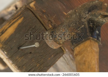 Old and worn contracting hammer and three nails on a distressed work bench