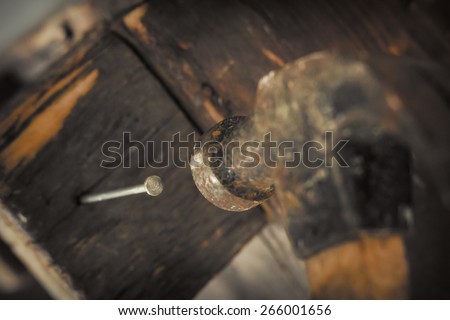 Old and worn contracting hammer and three nails on a distressed work bench