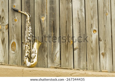 Lone old saxophone leans against wooden fence outside jazz club