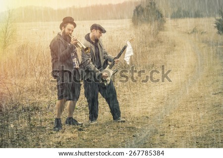 Stylish gypsies play trumpet and electric guitar on a wilderness path