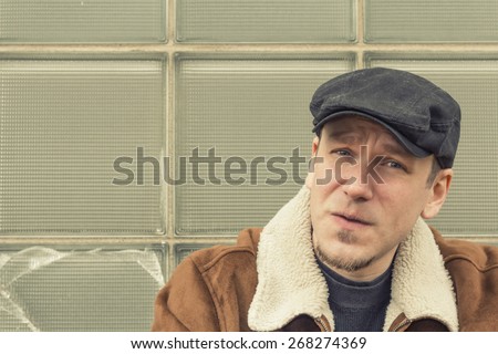 Cool guy in aviator jacket and newsie cap relaxes against a glass wall