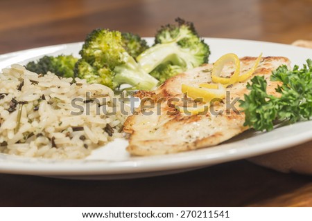 Crispy tender lemon chicken garnished with lemon twist with sides of herb wild rice and lemon broccoli