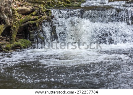 Waterfall rapids with water frozen in time splashing against mossy rocks